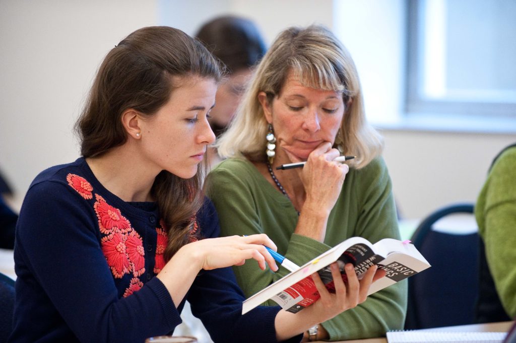 Women reading theology book together in classroom