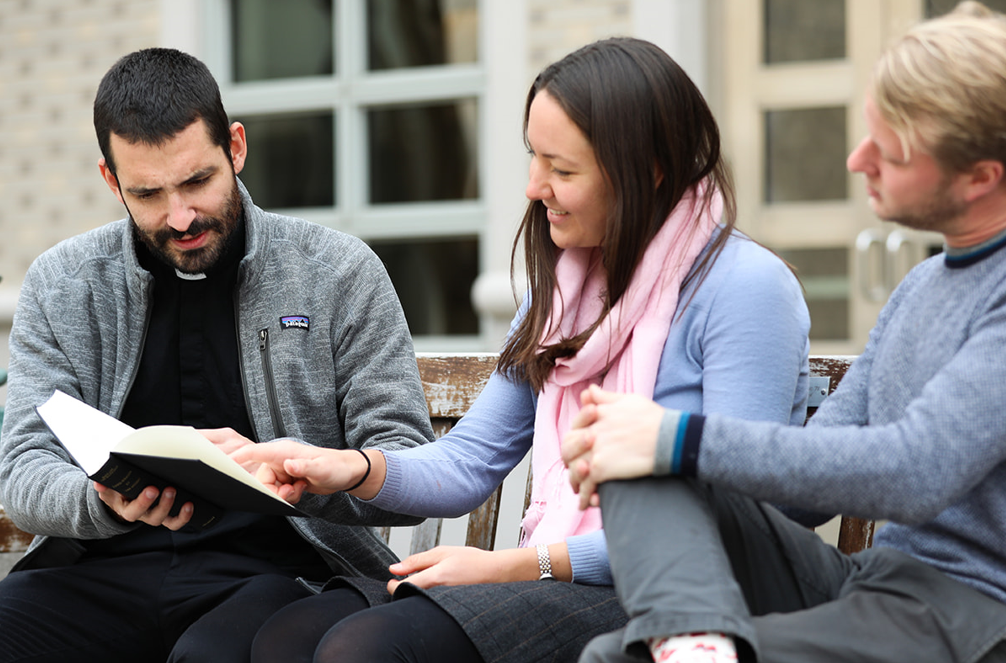 Catholic university students studying bible sitting together on bench outside